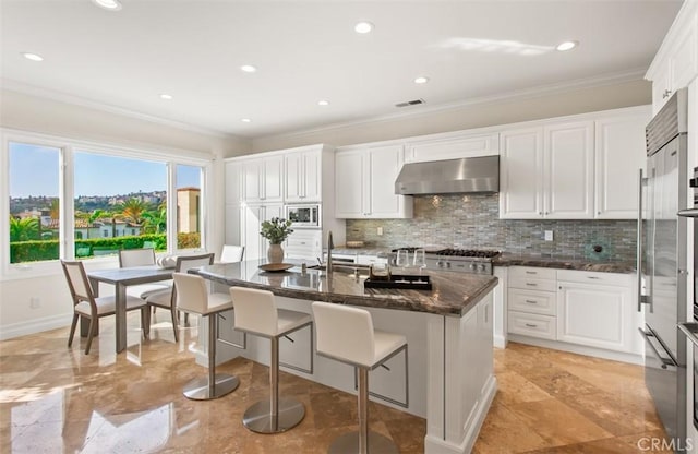 3 Atlantis Cv, Newport Coast, CA 92657 - kitchen featuring exhaust hood, ornamental molding, decorative backsplash, white cabinetry, and a kitchen breakfast bar