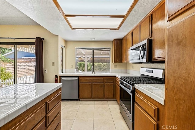 37702 Medea Ct, Palmdale, CA 93550 - kitchen featuring stainless steel appliances, tile counters, brown cabinets, and a textured ceiling