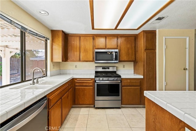 37702 Medea Ct, Palmdale, CA 93550 - kitchen with stainless steel appliances, brown cabinetry, light tile patterned floors, and tile countertops