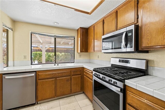 37702 Medea Ct, Palmdale, CA 93550 - kitchen with stainless steel appliances, brown cabinets, a textured ceiling, and light tile patterned floors