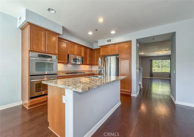 374 E Hilltop Way, Thousand Oaks, CA 91362 - kitchen featuring appliances with stainless steel finishes, dark wood finished floors, light stone counters, brown cabinets, and a center island with sink
