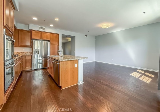 374 E Hilltop Way, Thousand Oaks, CA 91362 - kitchen with appliances with stainless steel finishes, dark wood finished floors, brown cabinetry, light stone countertops, and a kitchen island with sink