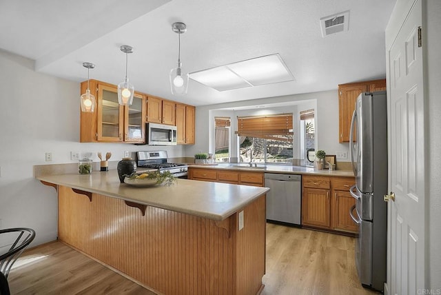 1930 Rosewood St, Vista, CA 92081 - kitchen featuring stainless steel appliances, a peninsula, a kitchen bar, brown cabinetry, and light wood finished floors