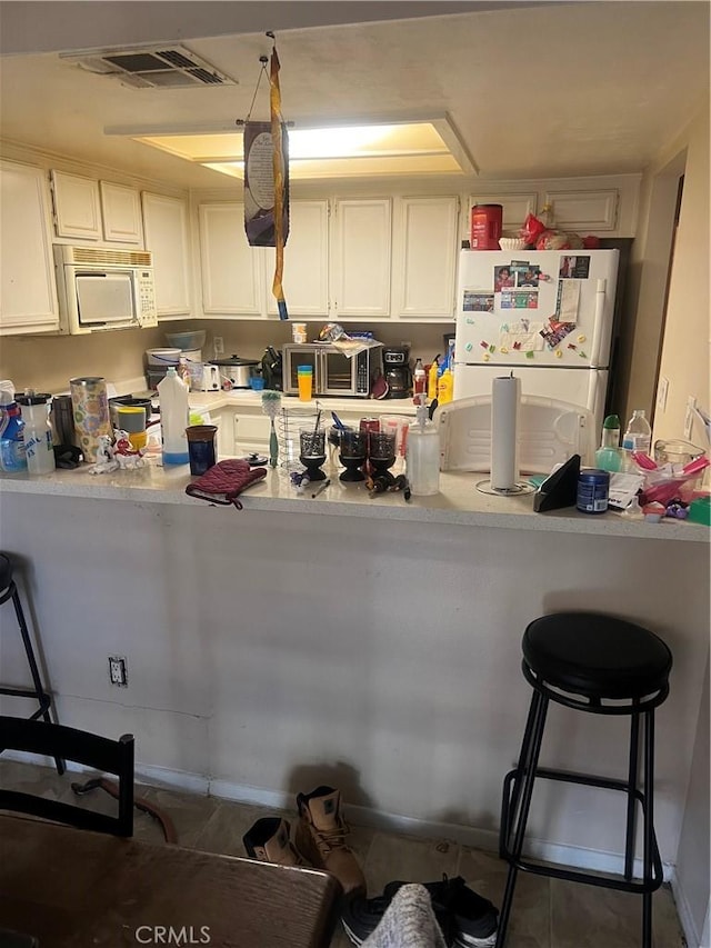 1025 N Tippecanoe Ave Unit 238, San Bernardino, CA 92410 - kitchen with white appliances, a peninsula, light countertops, a kitchen breakfast bar, and white cabinetry