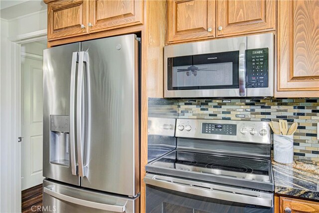 2164 Via Mariposa E Unit D, Laguna Woods, CA 92637 - kitchen with appliances with stainless steel finishes, tasteful backsplash, dark stone countertops, brown cabinetry, and ornamental molding