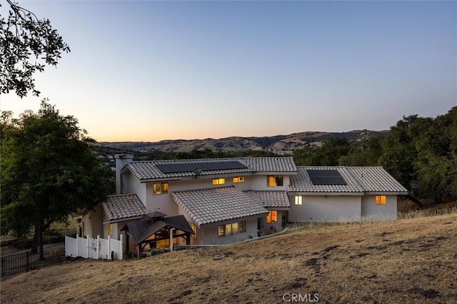 9230 Las Lomas Ave, Atascadero, CA 93422 - back of property at dusk with stucco siding, a mountain view, solar panels, and a chimney