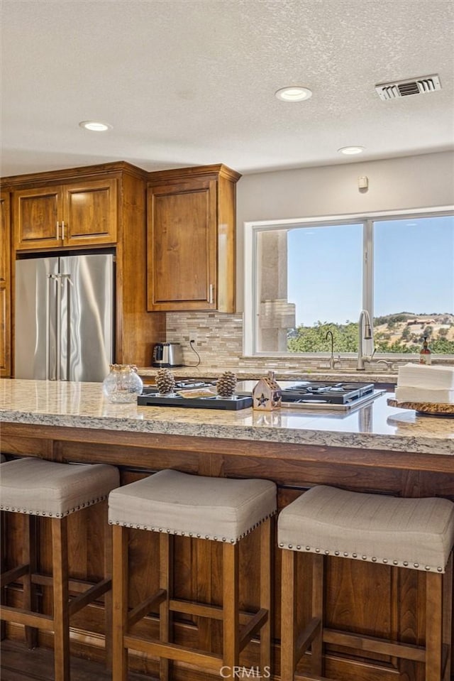 9230 Las Lomas Ave, Atascadero, CA 93422 - kitchen featuring stainless steel refrigerator, a breakfast bar, brown cabinets, decorative backsplash, and recessed lighting