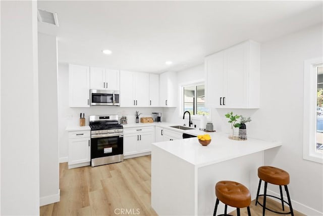 18746 Welby Way, Reseda, CA 91335 - kitchen featuring appliances with stainless steel finishes, a kitchen bar, light wood-type flooring, a peninsula, and white cabinets