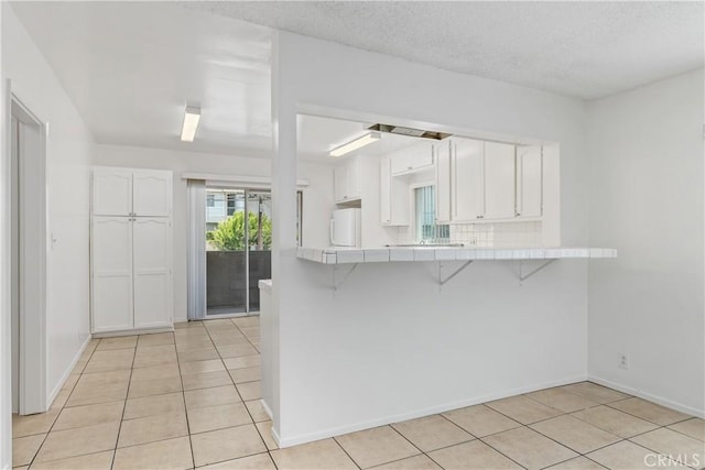 841 W 5th, San Pedro, CA 90731 - kitchen featuring tile counters, fridge, a breakfast bar area, light tile patterned floors, and white cabinets