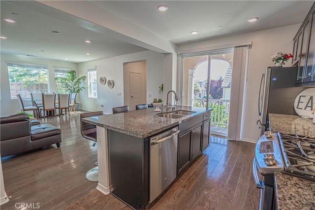 24270 Verdugo Cir, Valencia, CA 91354 - kitchen with stainless steel appliances, dark wood-style floors, dark stone counters, open floor plan, and an island with sink