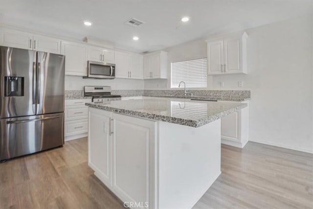 12956 9th Ave, Victorville, CA 92395 - kitchen with appliances with stainless steel finishes, white cabinetry, light wood-type flooring, a kitchen island, and light stone countertops