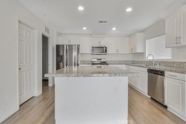 12956 9th Ave, Victorville, CA 92395 - kitchen featuring appliances with stainless steel finishes, white cabinets, a center island, light wood-style floors, and light stone counters