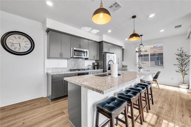 2123 Crescent Moon, Upland, CA 91786 - kitchen with appliances with stainless steel finishes, gray cabinets, light wood-type flooring, a kitchen island with sink, and a kitchen breakfast bar
