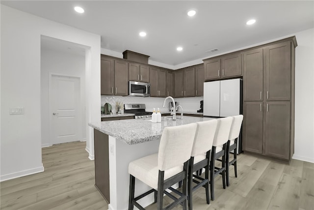 26149 Park Ave Unit 38, Loma Linda, CA 92354 - kitchen with appliances with stainless steel finishes, dark brown cabinets, light wood-style floors, an island with sink, and light stone counters