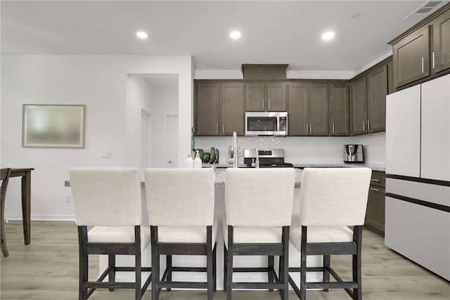 26149 Park Ave Unit 38, Loma Linda, CA 92354 - kitchen featuring stainless steel appliances, dark brown cabinetry, backsplash, a center island with sink, and a breakfast bar