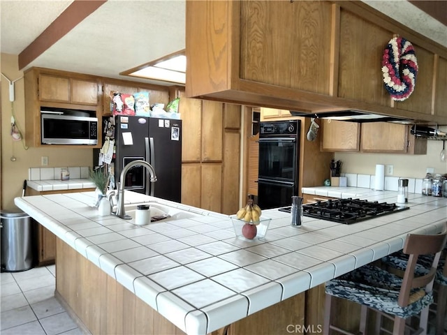 2390 Trinity Rd, Pinon Hills, CA 92372 - kitchen featuring black appliances, tile counters, light tile patterned floors, a peninsula, and brown cabinetry
