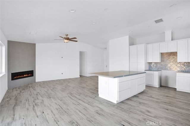 10533 Mohawk Rd, Apple Valley, CA 92308 - kitchen featuring white cabinetry, a fireplace, decorative backsplash, vaulted ceiling, and light wood-type flooring