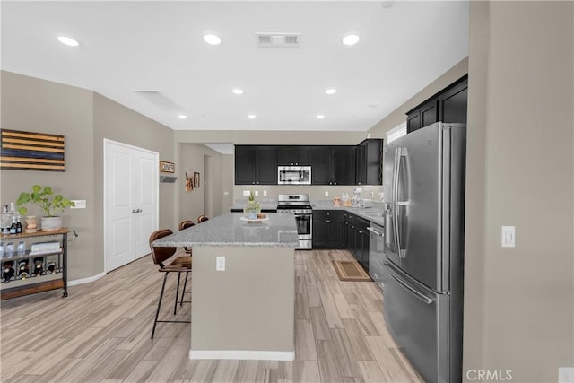 1511 Asteroid Way, Beaumont, CA 92223 - kitchen with stainless steel appliances, dark cabinets, a center island, light stone counters, and light wood-style floors