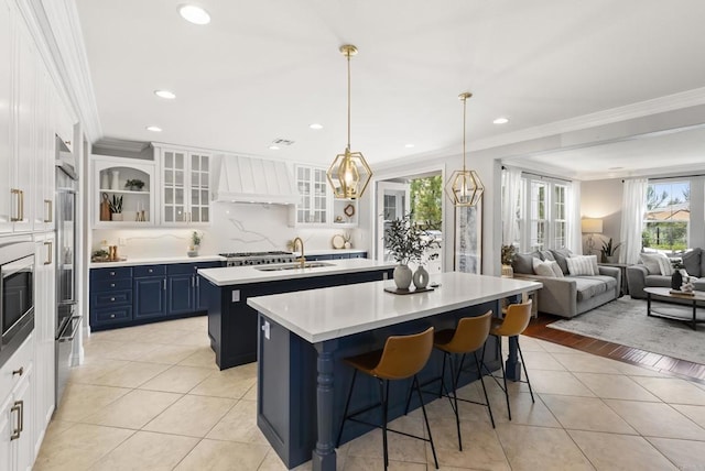 6257 Alverton, Carlsbad, CA 92009 - kitchen featuring premium range hood, a kitchen island with sink, crown molding, light tile patterned floors, and blue cabinets