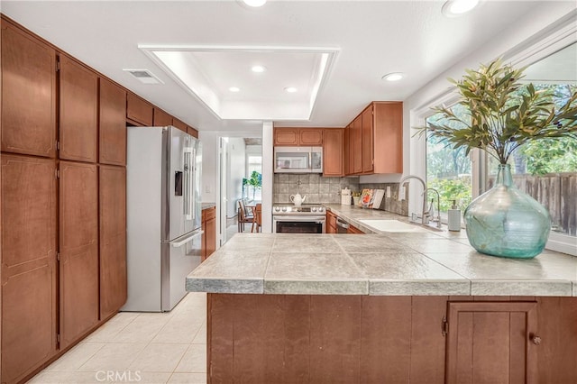 5022 Tamarack Way, Irvine, CA 92612 - kitchen featuring stainless steel appliances, brown cabinetry, decorative backsplash, a peninsula, and a tray ceiling