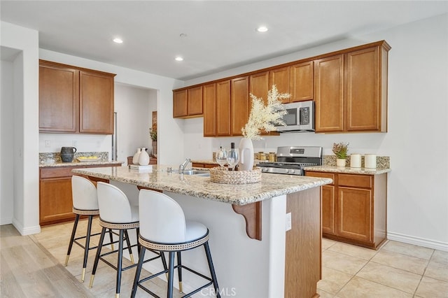 9370 Bistro Pl, Rancho Cucamonga, CA 91730 - kitchen with appliances with stainless steel finishes, brown cabinets, a kitchen island with sink, recessed lighting, and light stone counters