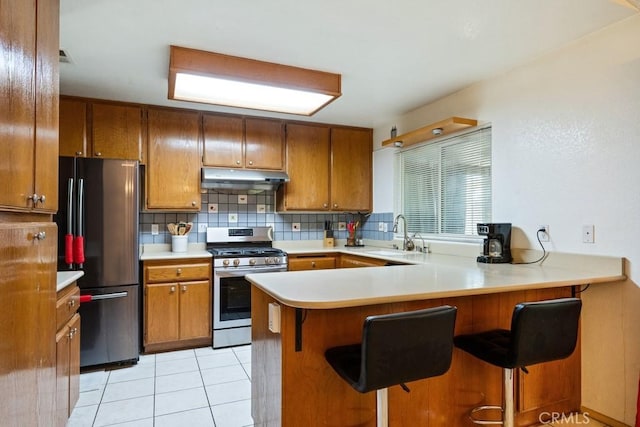 2549 Esperanza St, San Bernardino, CA 92410 - kitchen with stainless steel range with gas cooktop, freestanding refrigerator, under cabinet range hood, brown cabinets, and decorative backsplash