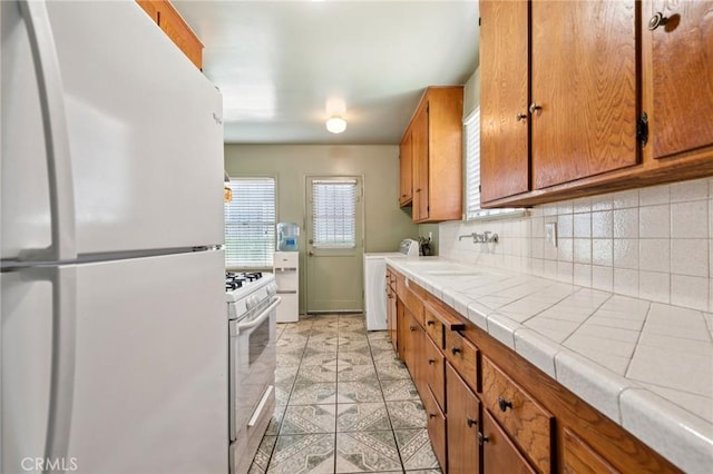 1908 W 134th Pl, Gardena, CA 90249 - kitchen featuring white appliances, tile counters, separate washer and dryer, brown cabinetry, and tasteful backsplash