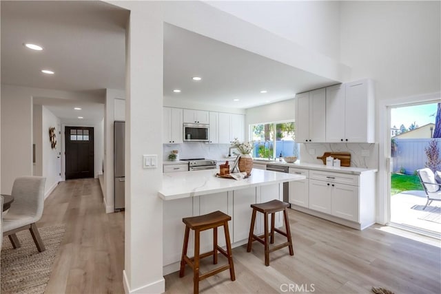 14632 Kimberly Cir, Tustin, CA 92780 - kitchen featuring stainless steel appliances, a kitchen bar, light wood-style floors, backsplash, and white cabinets