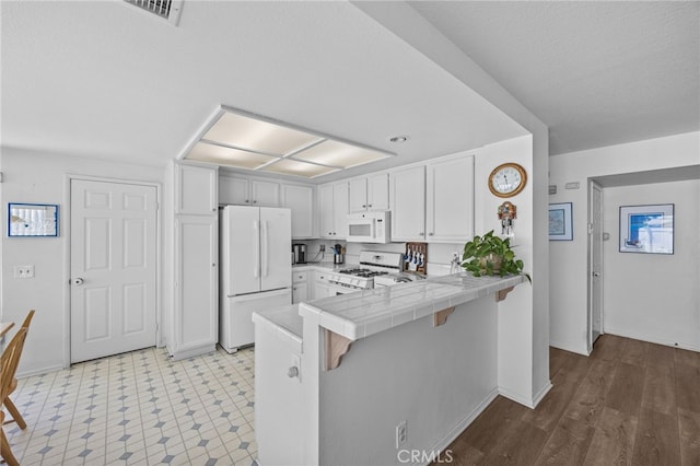 3681 Foxplain Rd, Corona, CA 92882 - kitchen with white appliances, tile counters, a peninsula, a kitchen breakfast bar, and white cabinets