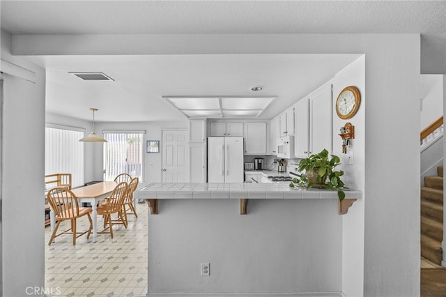 3681 Foxplain Rd, Corona, CA 92882 - kitchen featuring white appliances, tile counters, a peninsula, a breakfast bar area, and white cabinets