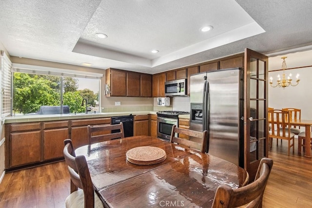 42724 Santa Suzanne Pl, Temecula, CA 92592 - kitchen with appliances with stainless steel finishes, a tray ceiling, wood finished floors, a textured ceiling, and a chandelier