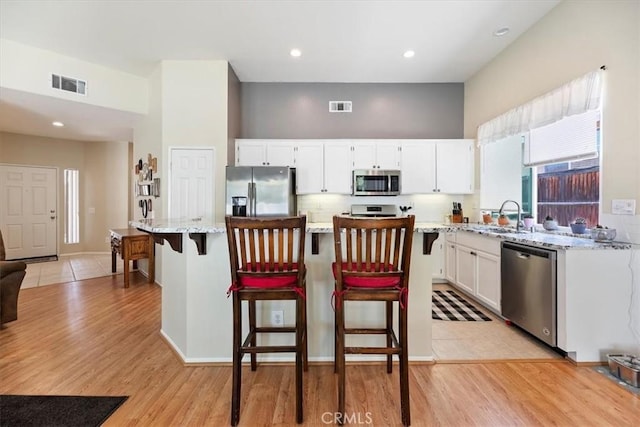 27185 Buffalo Trl, Corona, CA 92883 - kitchen with stainless steel appliances, white cabinetry, light wood-type flooring, light stone counters, and a center island