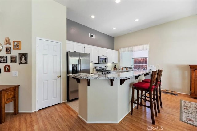 27185 Buffalo Trl, Corona, CA 92883 - kitchen featuring appliances with stainless steel finishes, light wood finished floors, a breakfast bar, light stone counters, and white cabinetry