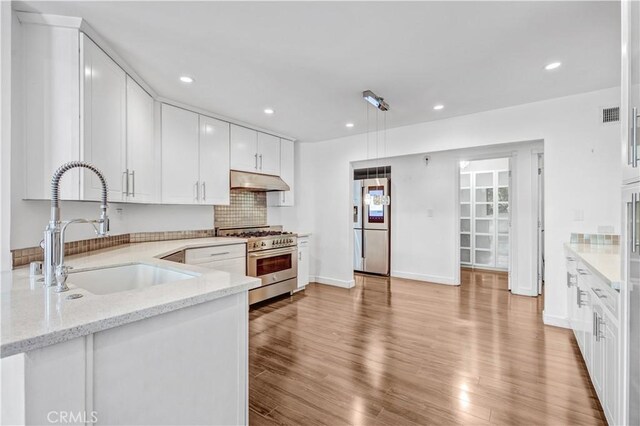5333 Zelzah Ave Unit 203, Encino, CA 91316 - kitchen featuring appliances with stainless steel finishes, under cabinet range hood, white cabinetry, light stone countertops, and light wood finished floors