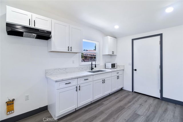 1235 Spruce St, San Bernardino, CA 92411 - kitchen featuring under cabinet range hood, white microwave, light wood-style flooring, white cabinets, and light stone countertops