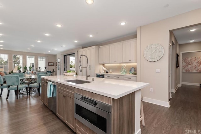 800 Grand Ave Unit 105, Carlsbad, CA 92008 - kitchen featuring appliances with stainless steel finishes, light countertops, open floor plan, dark wood-style flooring, and a kitchen island with sink