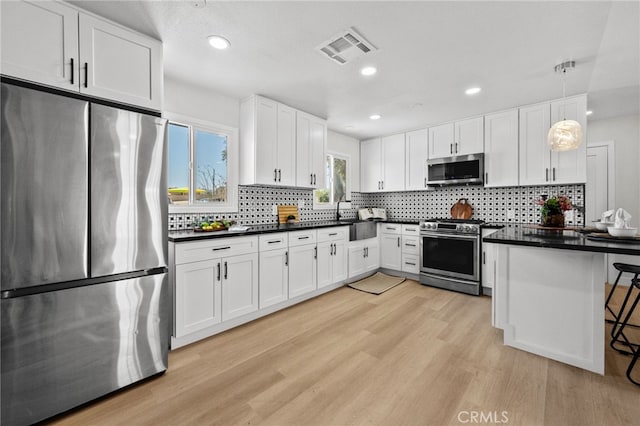 5676 Aztec Ave Unit 29, Palms, CA 92277 - kitchen with stainless steel appliances, dark countertops, white cabinets, light wood finished floors, and decorative backsplash