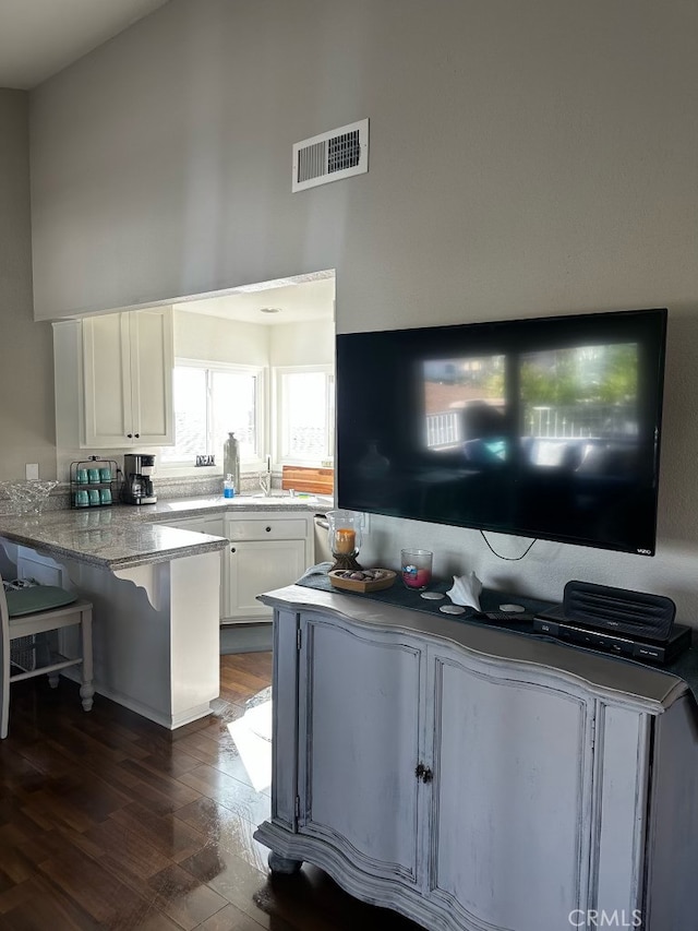 518 Avenida Victoria Unit A, San Clemente, CA 92672 - kitchen with a peninsula, white cabinets, dark wood-style floors, a breakfast bar, and light stone counters