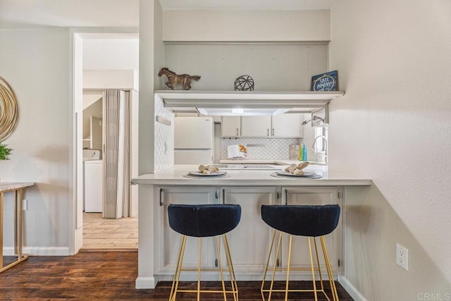 17177 Bernardo Center Dr, San Diego, CA 92128 - kitchen featuring freestanding refrigerator, dark wood-style flooring, backsplash, a peninsula, and washer / clothes dryer