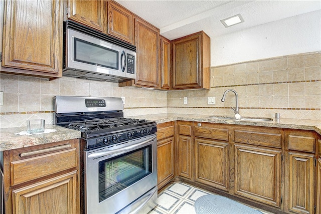 5050 Canyon Crest Dr Unit 5, Riverside, CA 92507 - kitchen with appliances with stainless steel finishes, brown cabinetry, decorative backsplash, a textured ceiling, and tile counters