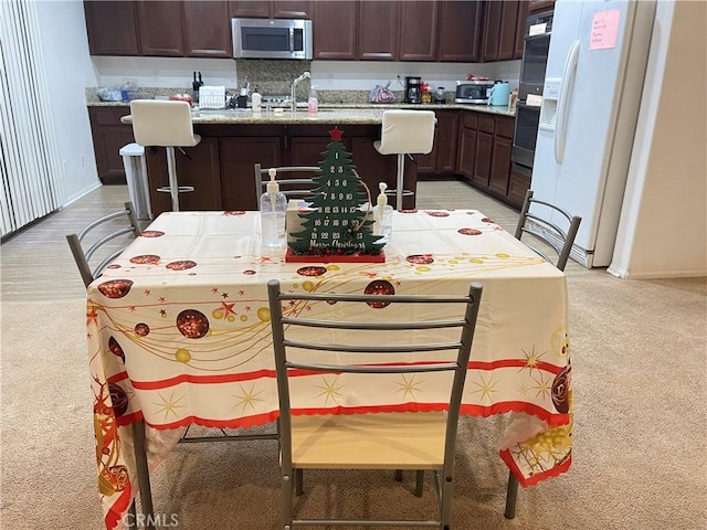 12639 Spruce Hill Rd, Moreno Valley, CA 92555 - kitchen featuring stainless steel appliances, light colored carpet, a center island with sink, and dark brown cabinets