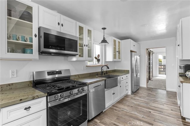 1164 12th St, Los Osos, CA 93402 - kitchen with stainless steel appliances, white cabinetry, light wood-type flooring, hanging light fixtures, and glass insert cabinets