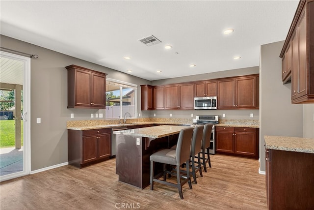 102 Mesa Ct, Calimesa, CA 92320 - kitchen with appliances with stainless steel finishes, light wood-style flooring, a kitchen island, a kitchen bar, and light stone countertops