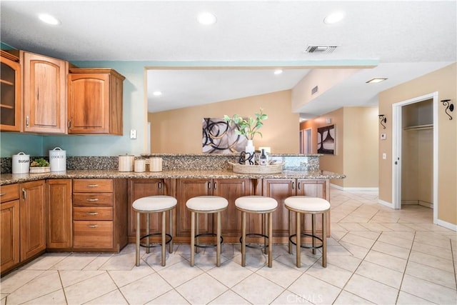 6910 Valinda Ave, Rancho Cucamonga, CA 91701 - kitchen featuring a breakfast bar area, stone counters, brown cabinets, glass insert cabinets, and a peninsula
