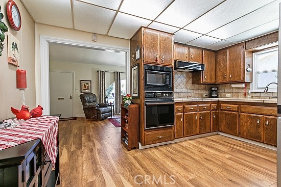 3110 N Greenbrier Rd, Long Beach, CA 90808 - kitchen with black appliances, ventilation hood, light wood-style floors, tile counters, and tasteful backsplash