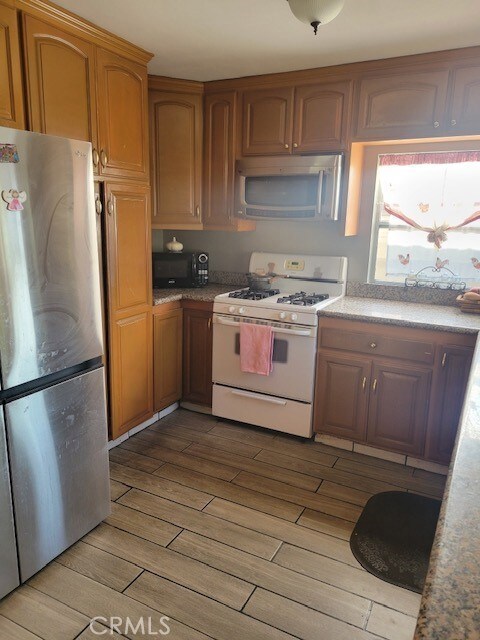 1140 W Cubbon St, Santa Ana, CA 92703 - kitchen featuring freestanding refrigerator, white range with gas cooktop, black microwave, light wood finished floors, and brown cabinets