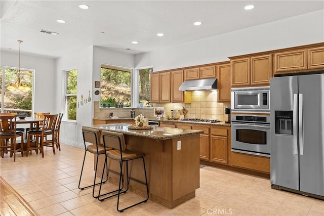 12703 Paso Verde Ct, Atascadero, CA 93422 - kitchen featuring stainless steel appliances, under cabinet range hood, brown cabinetry, dark stone countertops, and recessed lighting