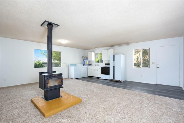 46404 Kings Canyon Rd, Lancaster, CA 93536 - unfurnished living room featuring washing machine and dryer, a wood stove, dark colored carpet, and a textured ceiling