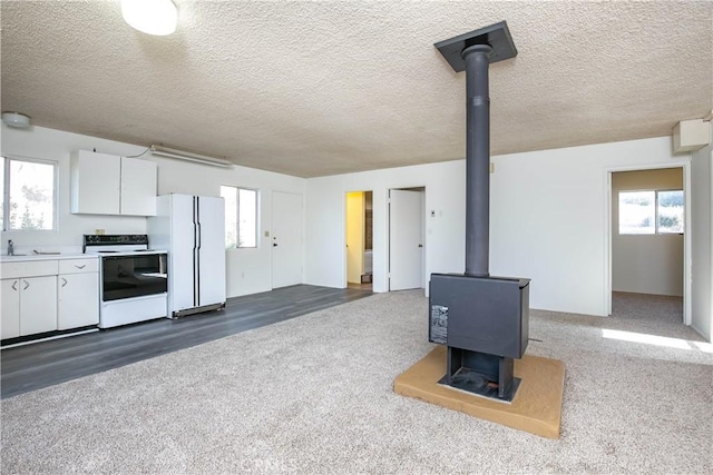 46404 Kings Canyon Rd, Lancaster, CA 93536 - unfurnished living room featuring a wood stove, dark colored carpet, and a textured ceiling