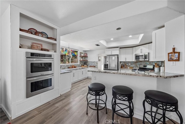 2981 Pembroke Cir, Corona, CA 92879 - kitchen with appliances with stainless steel finishes, open shelves, a peninsula, a raised ceiling, and light stone counters